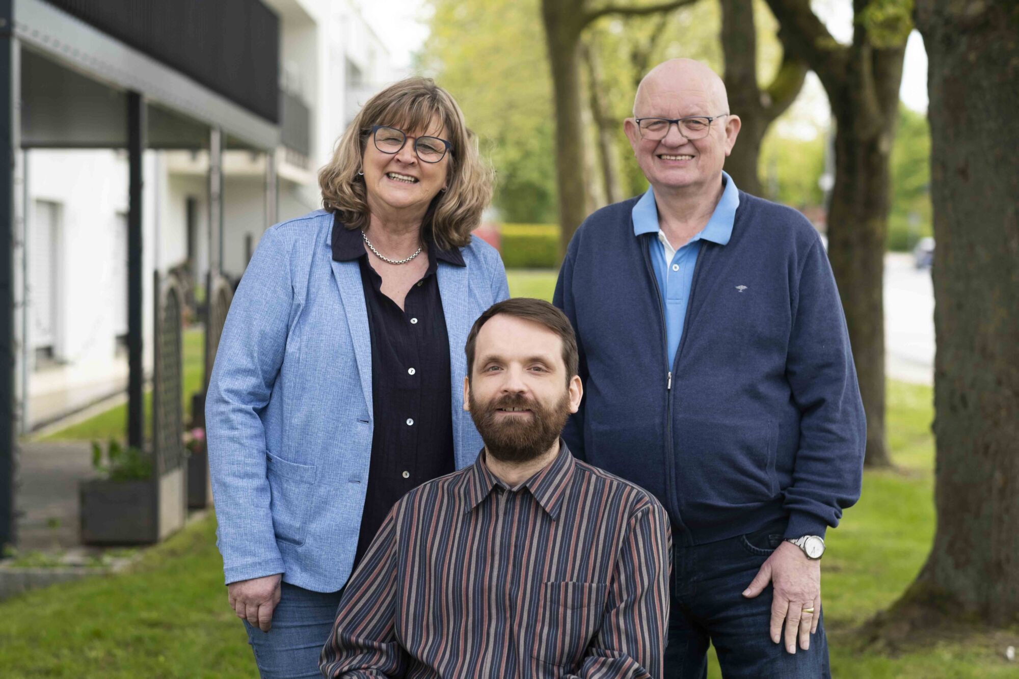 Marita Holper, Dennis Bando und Wiecher Braad lächeln in die Kamera, im Hintergrund unscharf das Wohnhaus an der Rombachstraße.