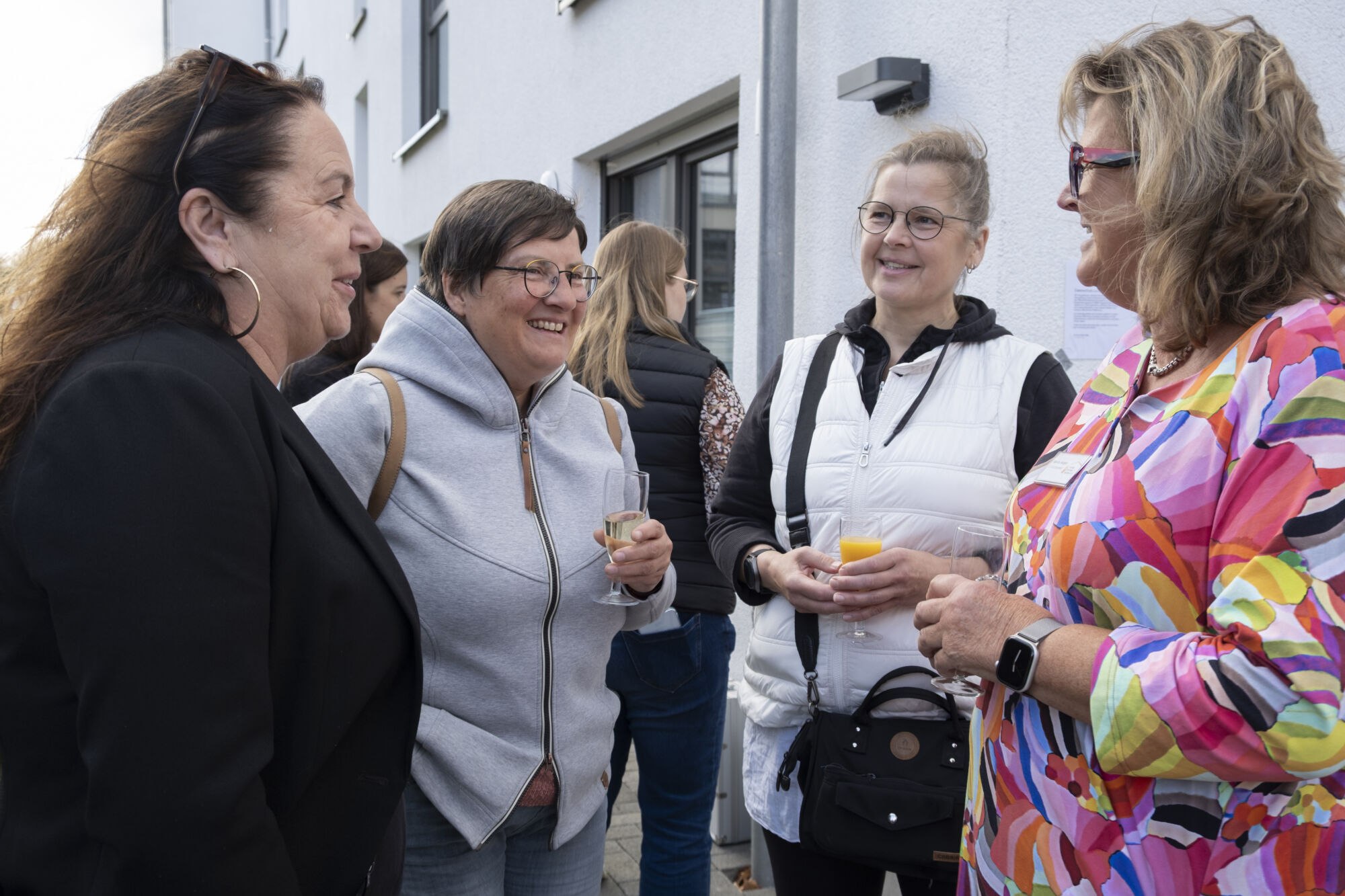 Persönliche Gespräche beim Richtfest und Tag der offenen Tür Vier Personen stehen im Freien zusammen, halten Getränke in den Händen und unterhalten sich.
